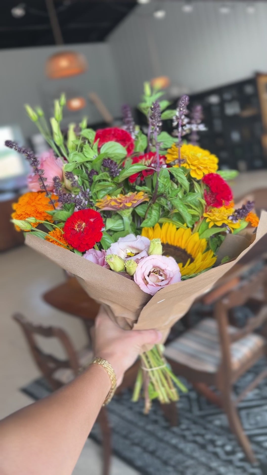 Video close-up of a hand-tied bouquet with sunflowers, red zinnias and pale pink flowers in kraft paper