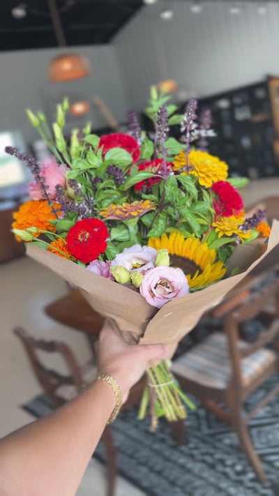 Video close-up of a hand-tied bouquet with sunflowers, red zinnias and pale pink flowers in kraft paper
